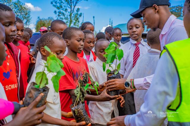 Schoolchildren holding tree seedlings up at Gathugu Primary School