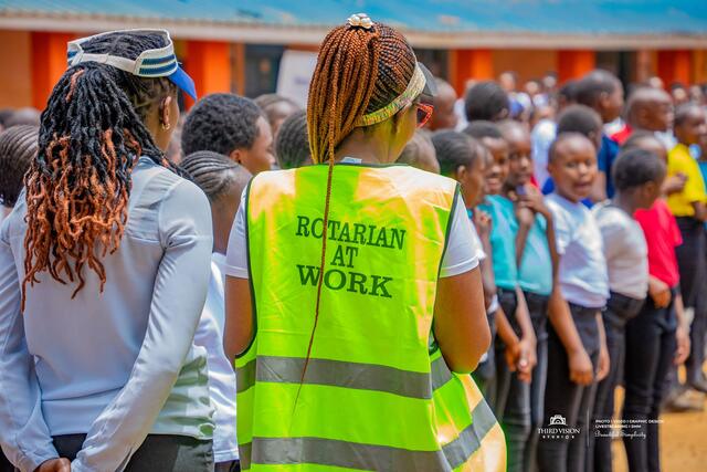 A volunteer in a Rotarian At Work vest among the assembled pupils